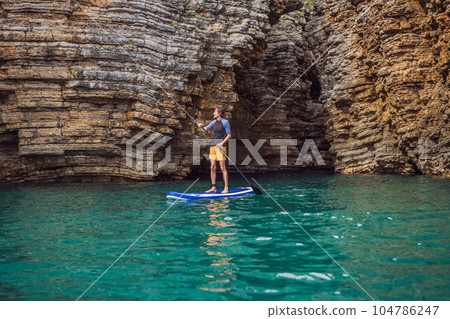 Young men Having Fun Stand Up Paddling in blue water seaamong the rocks in Montenegro. SUP 104786247