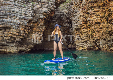 Young women Having Fun Stand Up Paddling in blue water seaamong the rocks in Montenegro. SUP Young women Having Fun Stand Up Paddling in blue water seaamong the rocks in Montenegro. SUP 104786248