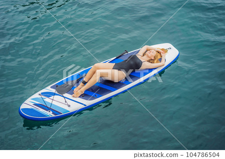 Young women Having Fun Stand Up Paddling in blue water seaamong the rocks in Montenegro. SUP 104786504