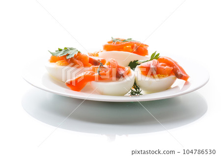 halves of boiled eggs with pieces of salted salmon on white background 104786530