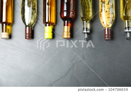 Different sorts of cooking oil in bottles on grey table, flat lay. Space for text Different sorts of cooking oil in bottles on grey table, flat lay. Space for text 104786659