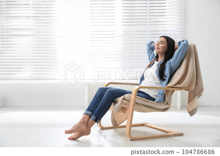 Young woman relaxing in armchair near window at home 104786686