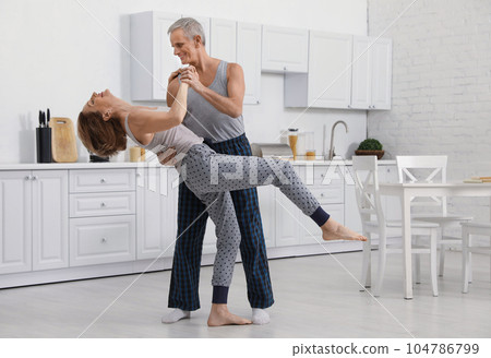 Happy senior couple dancing together in kitchen Happy senior couple dancing together in kitchen 104786799