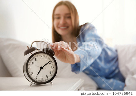 Young woman turning off alarm clock at home in morning, focus on hand 104786941