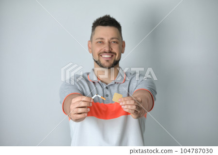 Happy man with nicotine patch and cigarette against light grey background, focus on hands 104787030
