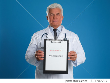 Doctor holding clipboard with words HEMORRHOID WE CAN HELP on blue background Doctor holding clipboard with words HEMORRHOID WE CAN HELP on blue background 104787207