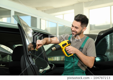 Worker tinting car window with heat gun in workshop Worker tinting car window with heat gun in workshop 104787213