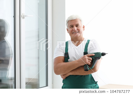 Mature repairman with electric screwdriver near plastic window indoors 104787277