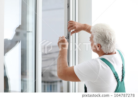 Mature construction worker repairing plastic window with screwdriver indoors 104787278