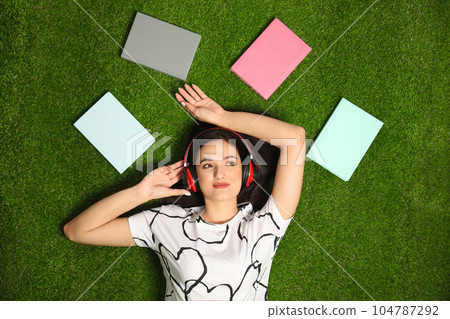 Young woman listening to audiobook while lying on grass, flat lay Young woman listening to audiobook while lying on grass, flat lay 104787292