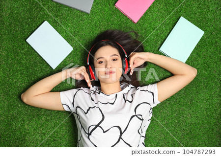 Young woman listening to audiobook while lying on grass, flat lay 104787293