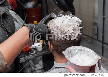 Hands of a professional barber in gloves in the process of coloring hair with dye at work in a hairdresser 104787388