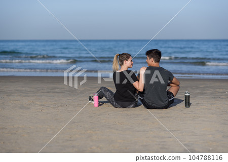 Young couple in love sitting on the rocky beach and looking on the horizon at sea. 104788116