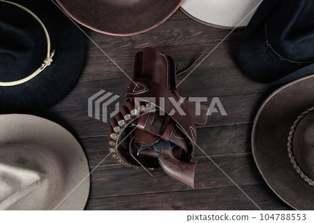 Gun with holster and gunbelt with old west hats on table. Top view. Gun with holster and gunbelt with old west hats on table. Top view. 104788553
