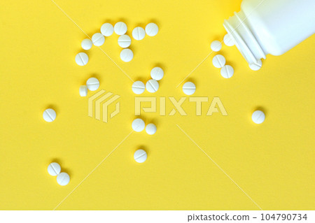 White pills spilled from white bottle with yellow background White pills spilled from white bottle with yellow background 104790734
