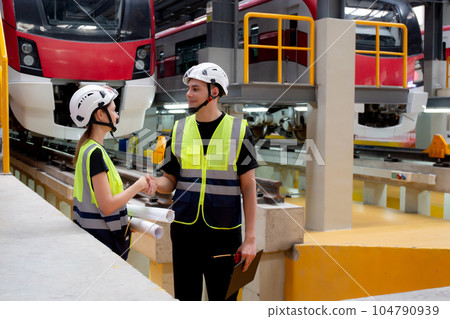 Young caucasian engineer man and woman hold blueprint meeting and checking electric train. 104790939