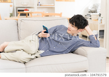 年輕人躺在沙發上看著他的智能手機 104791579