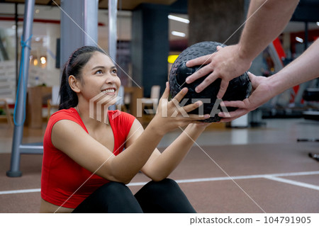 Young asian woman and caucasian man or trainer doing abs with ball with determination together. Young asian woman and caucasian man or trainer doing abs with ball with determination together. 104791905