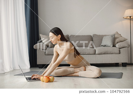 Slim and beautiful woman wearing beige leggins and top and sitting on yoga mat. Young girl with fit body posing at home with fresh apples. Sport, fitness, diet, nutrition and health care concept. Slim and beautiful woman wearing beige leggins and top and sitting on yoga mat. Young girl with fit body posing at home with fresh apples. Sport, fitness, diet, nutrition and health care concept. 104792566