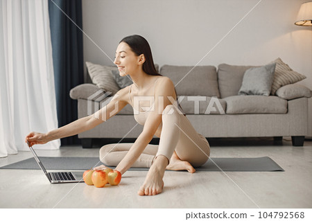 Slim and beautiful woman wearing beige leggins and top and sitting on yoga mat. Young girl with fit body posing at home with fresh apples. Sport, fitness, diet, nutrition and health care concept. 104792568