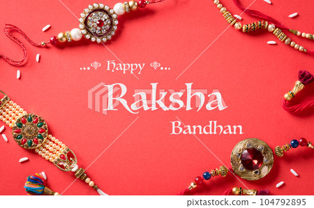 Raksha Bandhan, Indian festival with beautiful Rakhi and  Rice Grains on red background.  A traditional Indian wrist band which is a symbol of love between Sisters and Brothers. 104792895