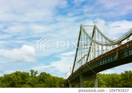 A modern pedestrian bridge, a lantern against a blue cloudy sky in summer day. A modern pedestrian bridge, a lantern against a blue cloudy sky in summer day. 104793837