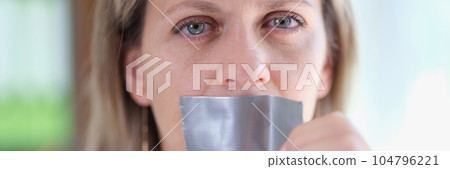 Young woman unsticking duct tape on mouth Young woman unsticking duct tape on mouth 104796221