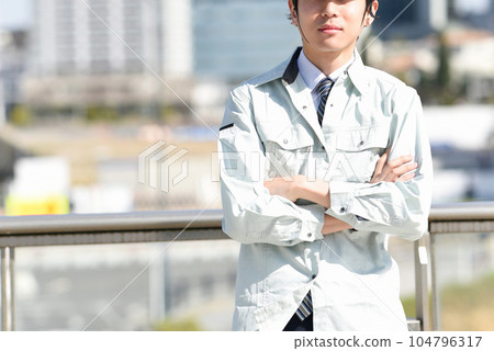 Young man in work clothes with arms folded Young man in work clothes with arms folded 104796317