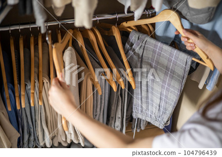 A woman chooses her trousers in the wardrobe. The concept of a harmonious capsule wardrobe. A woman chooses her trousers in the wardrobe. The concept of a harmonious capsule wardrobe. 104796439