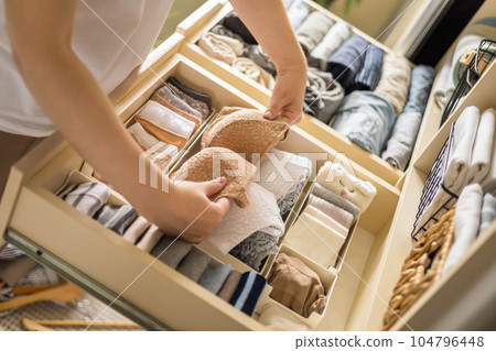 A young woman chooses which bra to wear while standing in front of a neatly arranged wardrobe. The concept of underwear storage and space organization. 104796448