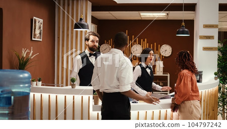 Tracking shot of african american tourists wanting to upgrade hotel stay, talking with helpful hotel personnel. Guests requesting extra room amenities not included in holiday package deal 104797242