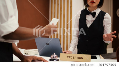 Asian receptionist offering african american business partners on work trip room access card key after finalizing check in. Tourists finishing booking process, close up dolly out shot Asian receptionist offering african american business partners on work trip room access card key after finalizing check in. Tourists finishing booking process, close up dolly out shot 104797305