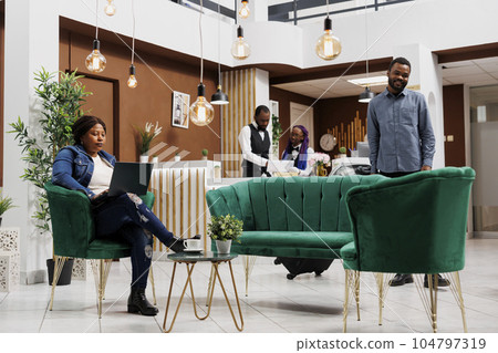 Focused African American woman freelancer sitting with laptop in hotel lobby, tourist using computer browsing internet while waiting to check in. Tourist using free wifi in lounge area at resort Focused African American woman freelancer sitting with laptop in hotel lobby, tourist using computer browsing internet while waiting to check in. Tourist using free wifi in lounge area at resort 104797319