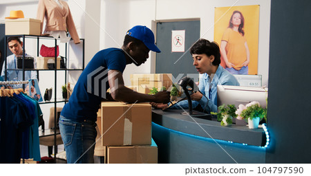 Asian manager asking courier to sign shipment report, discussing orders details in modern boutique. African american deliveryman bringing cardboard boxes to clothing store. Fashion concept 104797590