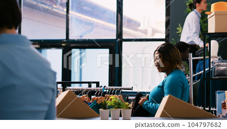 African american customer checking new fashion collection, analyzing clothes material before buying it. Shopaholic woman shopping for fashionable merchandise and accessories in modern boutique 104797682