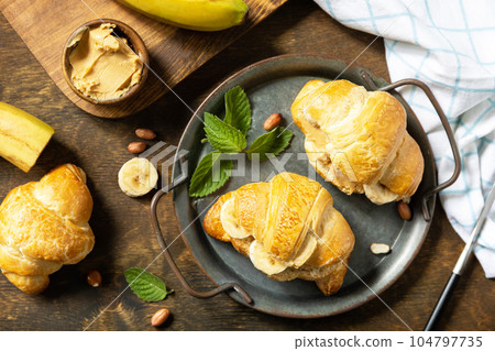 Healthy food dessert concept. French pastry. Tasty freshly baked croissants with peanut butter and banana on a rustic background. View from above. 104797735
