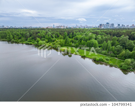 Big lake with green shores in bright sun light and city on horizon, aerial landscape. Recreation concept. Aerial view Big lake with green shores in bright sun light and city on horizon, aerial landscape. Recreation concept. Aerial view 104799341