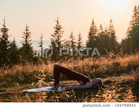 Pretty woman doing one leg bridge pose. Outdoors workout at early morning. Exercising on fresh air. Pretty woman doing one leg bridge pose. Outdoors workout at early morning. Exercising on fresh air. 104799933