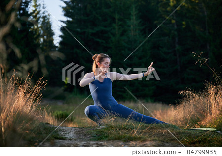 Sporty woman practicing yoga in forest. Middle-aged woman exercising early in morning. Female doing sport outdoor. Sporty woman practicing yoga in forest. Middle-aged woman exercising early in morning. Female doing sport outdoor. 104799935