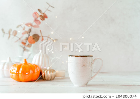 Details of Still life, cup of tea or coffee, pumpkins, candle, brunch with leaves on white table background, home decor in a cozy house. Autumn weekend concept. Fallen leaves and home decoration. 104800074