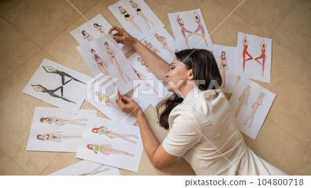 A woman lies on the floor and looks at sketches of swimwear and underwear.  104800718