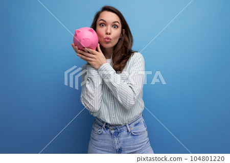 Joyful brunette young business woman in a shirt with a piggy bank on the background with copy pace 104801220