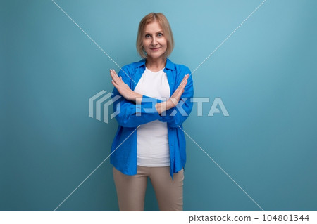portrait of a middle-aged blond woman in a casual stylish shirt with crossed arms on a blue 104801344