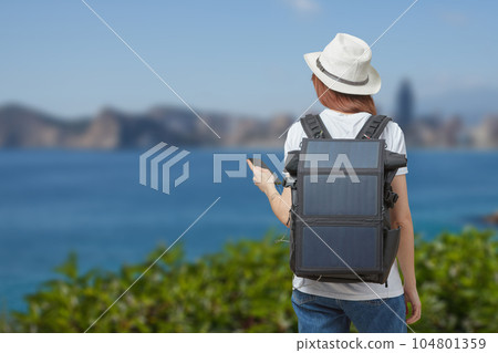 Young woman with mobile phone in hands and portable solar battery on background of river outdoors. 104801359