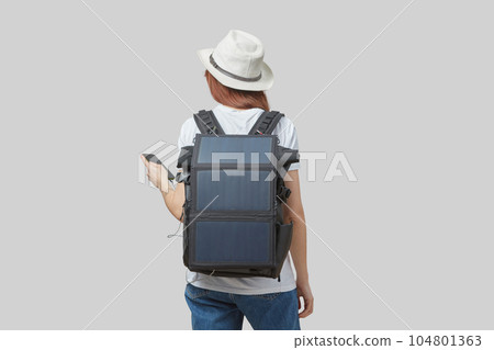 Girl carrying backpack with flexible solar panel attached to smartphone in her hands, isolated on light gray 104801363
