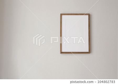 Vertical wooden picture frame mockup hanging on beige wall. Poster mock-upframe on pastel background in sunlight. Home interior with soft shadow, empty copyspace. Art display concept. Minimal interior 104802783