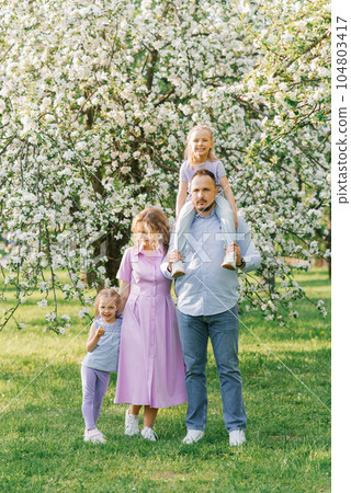 Young family with two girls and daughters on the background of a blooming garden Young family with two girls and daughters on the background of a blooming garden 104803417