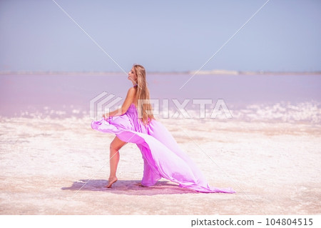Woman pink salt lake. Against the backdrop of a pink salt lake, a woman in a long pink dress takes a leisurely stroll along the white, salty shore, capturing a wanderlust moment. Woman pink salt lake. Against the backdrop of a pink salt lake, a woman in a long pink dress takes a leisurely stroll along the white, salty shore, capturing a wanderlust moment. 104804515