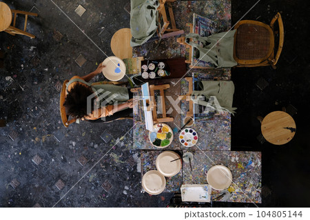 Aerial view of female artist painting picture on canvas in dark creative studio. Art, education and creative hobby concept Aerial view of female artist painting picture on canvas in dark creative studio. Art, education and creative hobby concept 104805144
