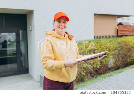 Happy Delivery woman with parcel in hand sending parcel to customer front of the house from shopping online with good service. Courier send a package to destination. 104805333